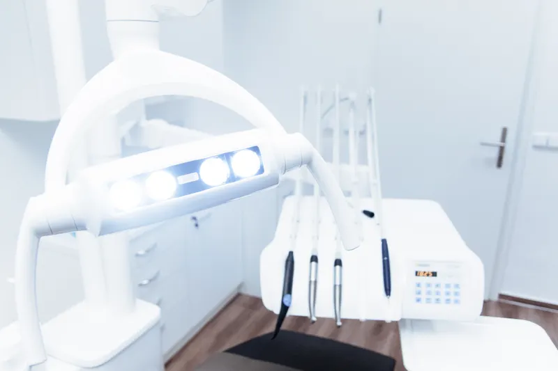 A bright, clean dental treatment room with a white chair, light and instruments.