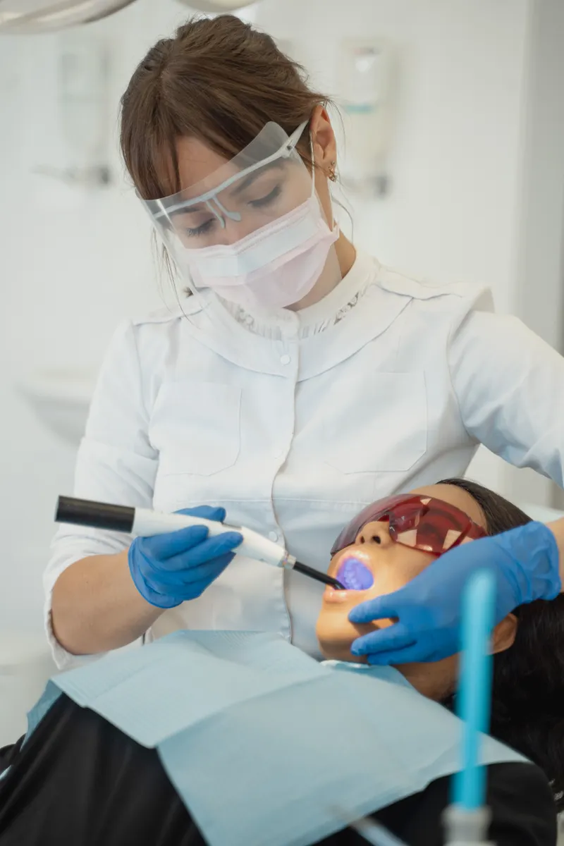A dentist uses a small blue light to harden a filling while the patient wears tinted glasses.